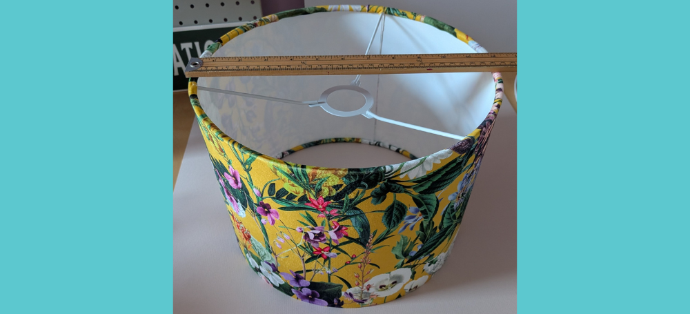 photo shows a lampshade covered in floral fabric on a yellow background with a tape measure on top